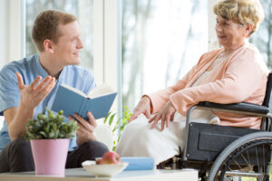 Care assistant reading a book to an elder wheelchair user